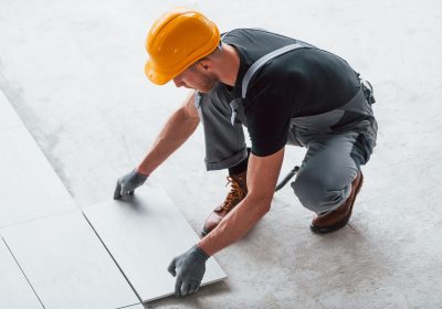 Installation of plate. Man in grey uniform and orange hard hat works indoors in modern big office at daytime.
